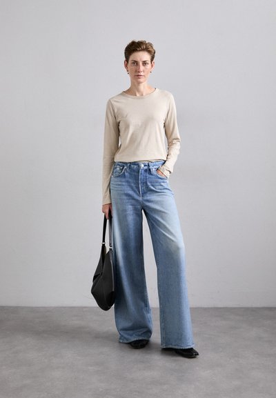 Beige long-sleeve top paired with light blue wide-leg jeans. Accessories include a black handbag and black shoes. Simple, minimal design.