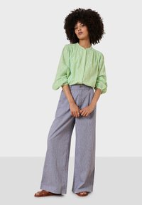 Light green, textured blouse with puff sleeves and a button closure, paired with wide, striped trousers and brown flat sandals.