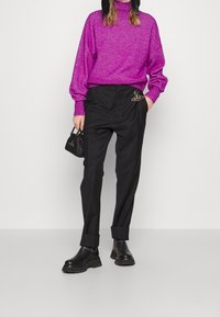 Pull à col roulé violet en maille épaisse, pantalon noir ajusté avec ourlets retroussés et bottines plateformes en cuir noir. Petit sac à main noir.