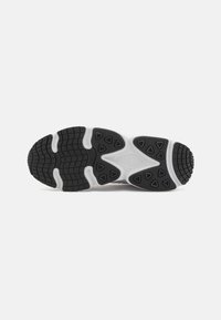Black rubber sneaker sole with multi-directional traction pattern, featuring textured segments and triangular grip accents. White midsole outline.