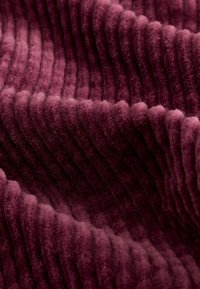 Un tissu en velours côtelé bordeaux présentant des côtes prononcées, une texture douce et un aspect velouté, créant profondeur et intérêt visuel.
