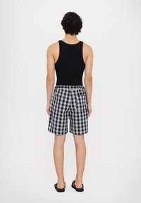 Svart tanktopp kombinert med knelange marineblå og hvite rutete badeshorts, med en avslappet passform og elastisk midjebånd. Sandaler er synlige.