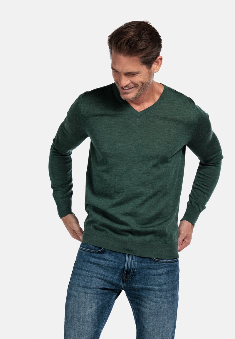 Groene v-hals trui van zacht, gebreid materiaal met lange mouwen, gecombineerd met blauwe spijkerbroek. Heeft een ontspannen pasvorm en een casual ontwerp.