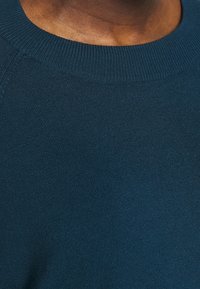 Tessuto di maglione blu navy a maglia con collo a coste e superficie liscia. La vista ravvicinata evidenzia il motivo delle cuciture uniforme.