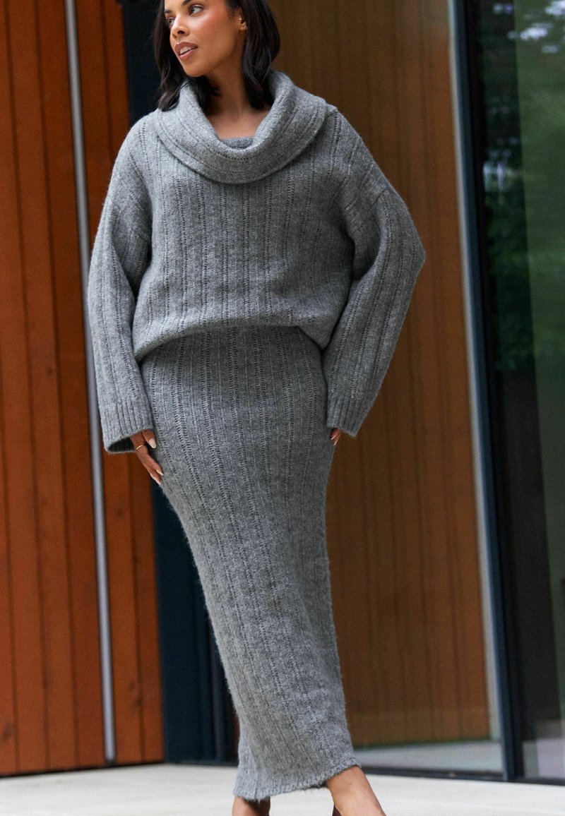 Grauer Strickpullover mit weitem Stehkragen und geripptem Textur, kombiniert mit einem passenden, gerippten Rock, beide mit einer schlanken, figurbetonten Silhouette.