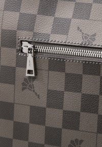 Puzdro na zips má šedý kostkovaný vzor z texturovaného materiálu se zipem v barvě stříbra a minimálními detaily značky.