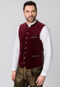 Burgunderfarbenes Samtwesten mit grauen Akzenten, sechs Knöpfen und horizontalen Taschenbesätzen. Getragen über einem weißen Hemd mit Kragen, kombiniert mit dunklen Hosen.