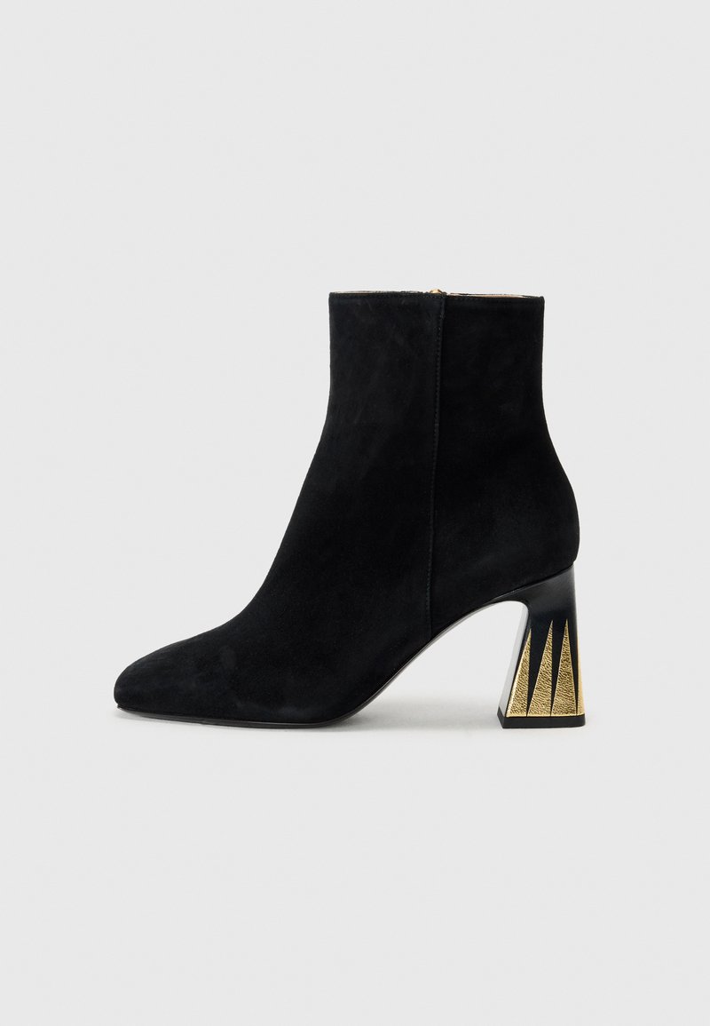 Bottine en suède noir avec un bout pointu et un talon bloc géométrique texturé en or et noir. Fermeture éclair à l'arrière.