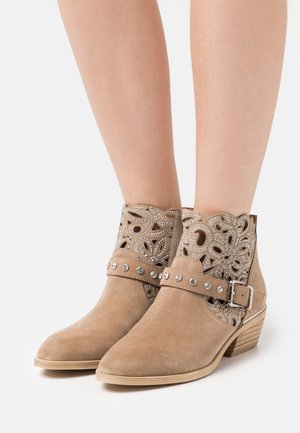 Botines de ante color canela con diseño floral recortado, adornos con tachuelas y hebilla. Tacón bajo apilado y suela lisa para mayor estabilidad.