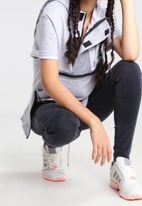 Gray zip-up hooded top with black accents, gray pocket, and short sleeves, paired with black pants and white sneakers with pink soles.