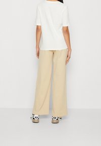 Vit t-shirt med kort ärm kombinerad med beige vida byxor; svarta och vita sneakers med en accentuerad logga på sidan.