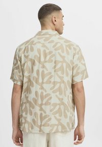 Chemise à manches courtes de couleur beige clair avec un motif abstrait évoquant du corail, fabriquée en tissu doux et texturé avec une coupe décontractée.