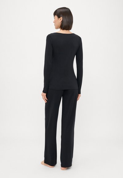 Melna garo piedurkņu blūze un saskaņotas bikses, kas izgatavotas no mīksta, elastīga auduma. Pieguļošs dizains ar taisnām kājām un minimālu apdari.