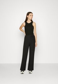 Μαύρο τοπ χωρίς μανίκια συνδυασμένο με ψηλόμεσα μαύρα παντελόνια που διαθέτουν ζώνη. Το σύνολο έχει απαλό υφασμά και χαλαρή γραμμή. Φοριέται με αθλητικά παπούτσια.