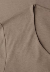 Detailní záběr na béžovou látku s ušitým trojúhelníkovým výřezem a viditelným švem podél okrajů.