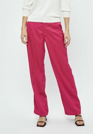 Pantalons larges en satin rose avec une texture lisse et une coupe ajustée, associés à un pull blanc et des sandales noires à lanières.