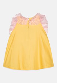 Robe sans manches jaune avec un col à volants à pois roses, fermeture à boutons dans le dos et texture en coton lisse.