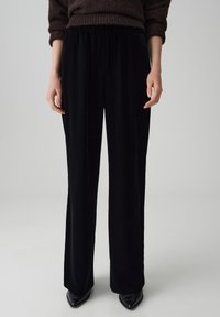 Zwarte fluwelen broek met een elastische tailleband, wijd been ontwerp en een soepele textuur, gecombineerd met zwarte puntige hakken.