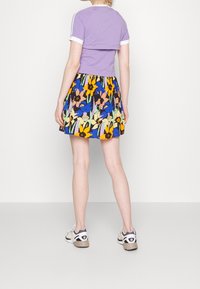 Lilla cropped top med hvide accenter, parret med en multifarvet nederdel med blomsterprint. Indeholder livlige farver og legende designs.