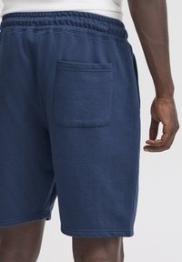 Tmavomodré bavlnené šortky s elastickým pásom a zadným záplatovým vreckom. Hladká textúra s voľným strihom a čistým lemom.