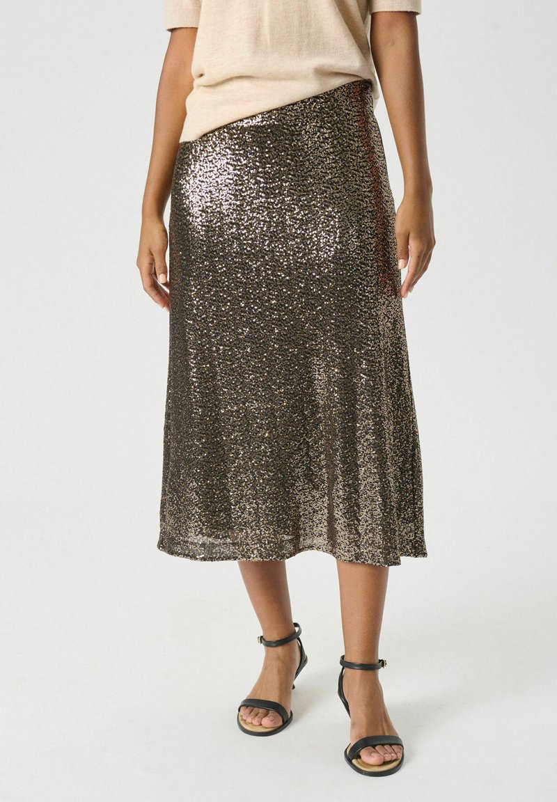 Gonna midi luminosa di colore bronzo con una vestibilità ampia, caratterizzata da una sottile texture di paillettes e uno spacco laterale, abbinata a sandali neri con cinturini.