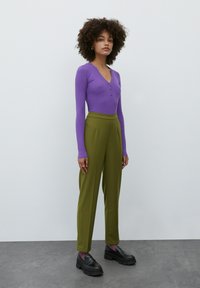 Paarse geribbelde longsleeve top met een V-hals en knoopdetail, gecombineerd met hoog-waist olijfgroene broek en zwarte robuuste loafers.