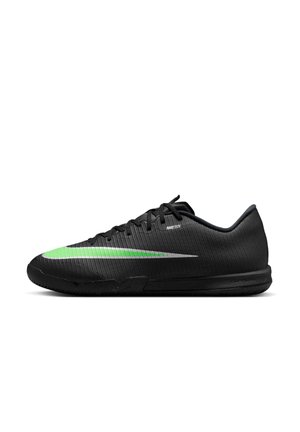 Chaussure de sport noire basse avec une bande verte et blanche sur le côté et des lacets noirs sur fond blanc.