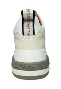 Baskets blanches avec une semelle grise texturée et un détail de logo contrastant sur l'onglet de talon rembourré. Présente un dessus lisse et de fines rayures noires.