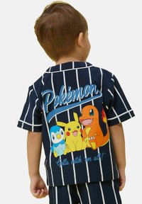 Jūrų laivyno trumpomis rankovėmis marškiniai su baltais raštais, kuriuose pavaizduoti „Pokémon“ grafikai, įskaitant Pikachu, Piplup ir Charmander, o gale yra užrašas „Pokémon“. 