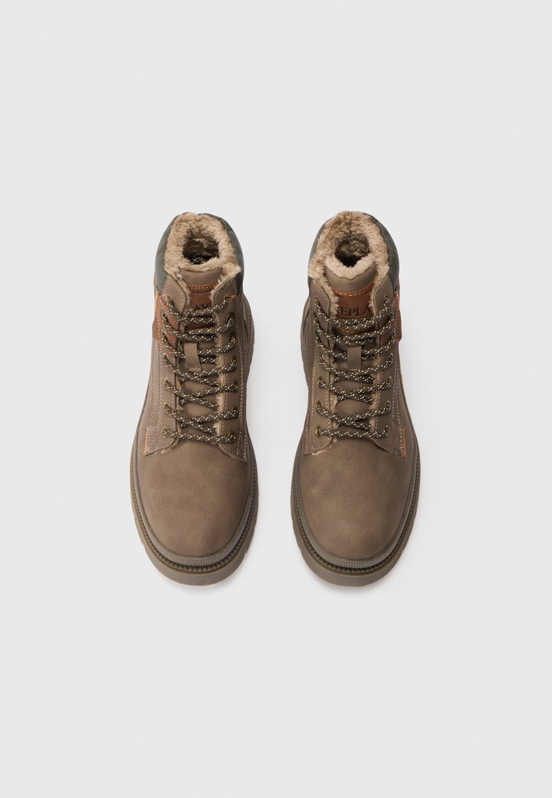 Un paio di stivali invernali marroni con lacci, foderati in pelliccia e suole robuste, visti dall'alto su uno sfondo bianco.