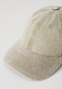 Cappellino da baseball beige chiaro realizzato in tessuto testurizzato, con visiera curva e dettagli di cucitura visibili lungo le cuciture e il corpo del cappello.