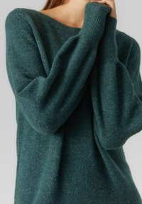 Grön stickad tröja med avslappnad passform, bred halsringning och långa, något böljande ärmar. Tillverkad av ett mjukt, texturerat material.