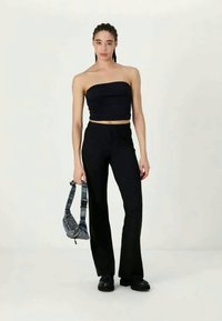 Haut bandeau noir associé à un pantalon noir taille haute. La mannequin tient un sac gris texturé avec une bandoulière. Tissu lisse, design minimaliste.