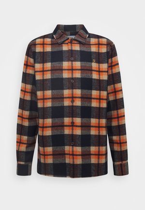 Chemise à manches longues avec boutons, motif à carreaux orange, noir, beige et marron, et petit logo brodé sur la poitrine gauche.