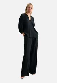 Blusa nera ampia con scollo a V, maniche arricciate e tessuto morbido abbinata a pantaloni neri a gamba larga. Design semplice e monocromatico.