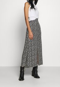 Sort blomster maxi skirt med en slids, prydet med små hvide blomster og et flowy design. Sammen med en hvid ærmeløs top og sorte hælede støvler.