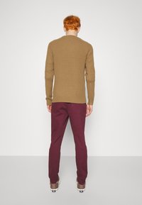 Suéter de canalé marrón claro combinado con pantalones burdeos y zapatillas grises. El conjunto tiene un corte ajustado y un diseño simple pero texturizado.