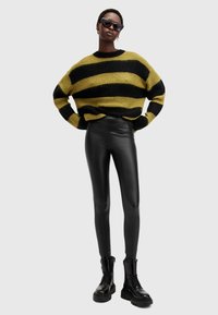 Maglione a righe nere e gialle, vestibilità ampia, abbinato a leggings neri in finta pelle a vita alta e stivali neri con lacci spessi.