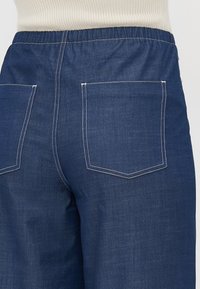 Elastisk midje denimbukser i mørkeblå med hvite sømmer, med to baklommer og en glatt tekstur.