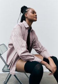 Light pink striped oversized shirt with a button-down design, paired with black thigh-high socks, seated on a transparent acrylic chair.