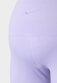 Fialové legíny vyrobené z elastického materiálu, s bezšvovým dizajnom a malým strieborným logom Nike blízko pása pre branding.