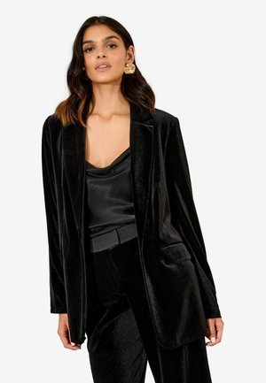 Schwarzer Samtblazer mit Schalkragen, einer einzigen vorderen Tasche und langen Ärmeln, kombiniert mit einem schwarzen Satin-Camisole. Glatte Textur, elegantes Design.