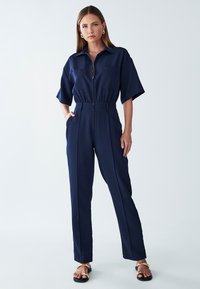 Navyblauw jumpsuit met een rits aan de voorkant, korte mouwen en een cinched taille, voorzien van twee voorzakken en een op maat gemaakte, rechte pijpdesign.