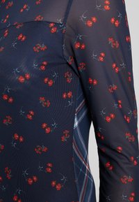 Navy mesh top featuring a floral pattern in red and blue. Includes a plaid accent on the side. Lightweight with a textured finish.