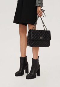 Black quilted handbag with silver hardware and chain handle, paired with black ankle booties featuring chunky heels and textured soles.