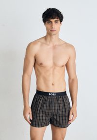Kariert Boxershorts in Schwarz, Braun und Orange, mit einem schwarzen Bund mit "BOSS" Logo. Hergestellt aus weichem Stoff mit lockerer Passform.
