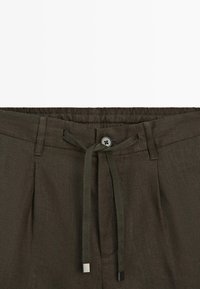 Mørkeolivengrønne bukser med elastisk talje, knaplukning, bæltestropper og en matchende snor bundet i en sløjfe foran.