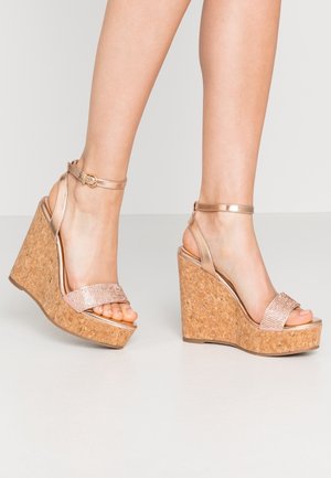 Sandales compensées en or rose métallique avec plateforme en liège, présentant une bride ornée de cristaux et une boucle de cheville réglable.
