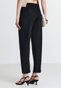 Pantaloni neri, leggeri e larghi con superficie testurizzata, vita elasticizzata e orli arrotolati. Indossati con tacchi neri a strappo.