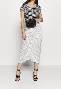 Haut à motifs noir et blanc avec manches courtes, associé à une jupe blanche à pois de longueur mi-mollet. Talons noirs à brides et petit sac noir.